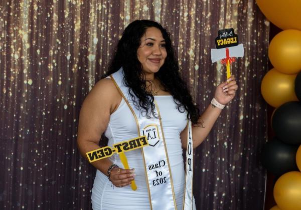 A person holding "First-Gen" and Building Legacy photo props while standing in front of a glittery curtain.