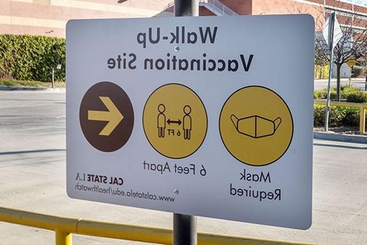 疫苗接种地点的步行标志建议游客戴口罩并保持6英尺的距离